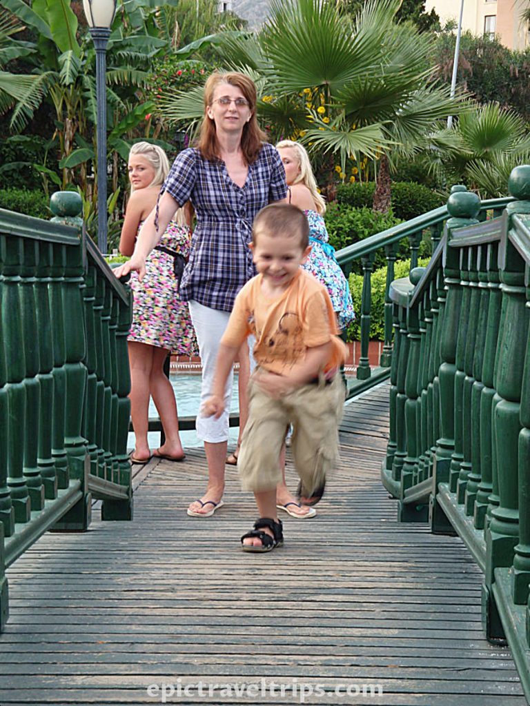 Boy runs over the wooden bridge with mom at the back in the park garden