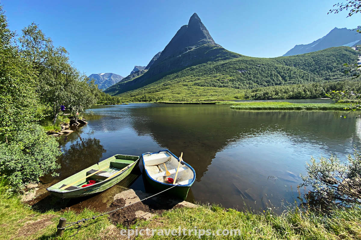 Blue-sky sunny day, with two boats on the lake shore and mountain peaks in the background. Renndølsetra summer farm house at Innerdalen valley in Norway.
