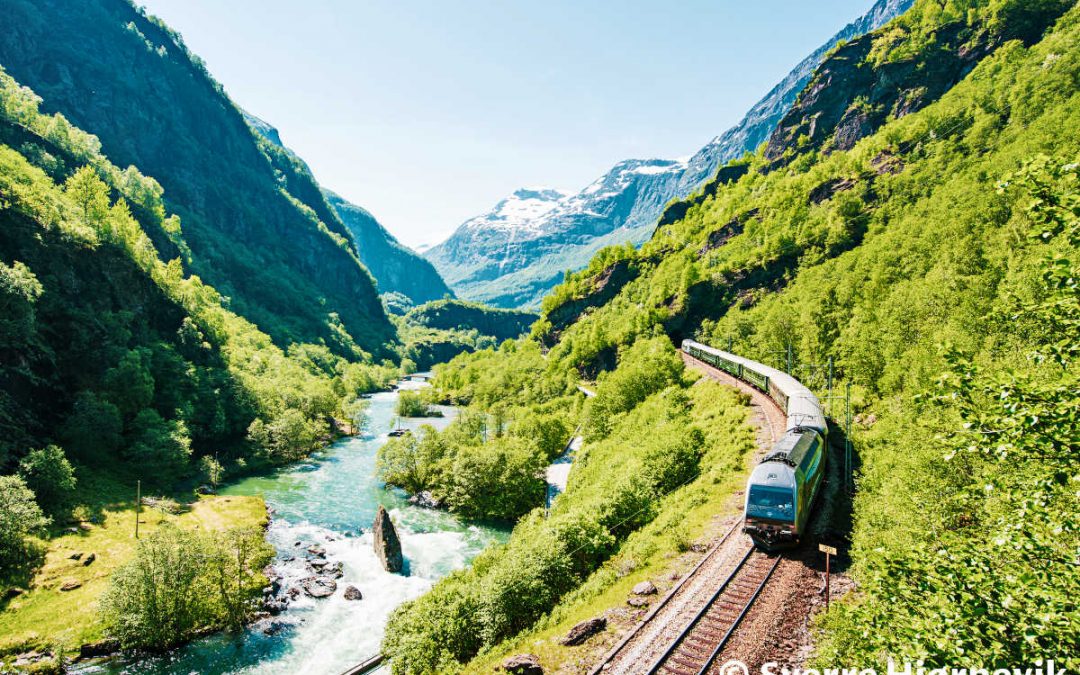 Flåm train between the mountains near the beautiful river in Norway.