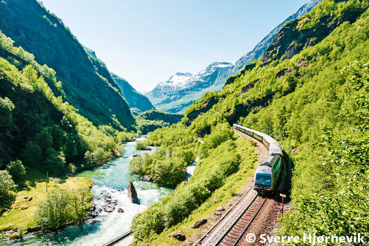 Flåm train between the mountains near the beautiful river in Norway.