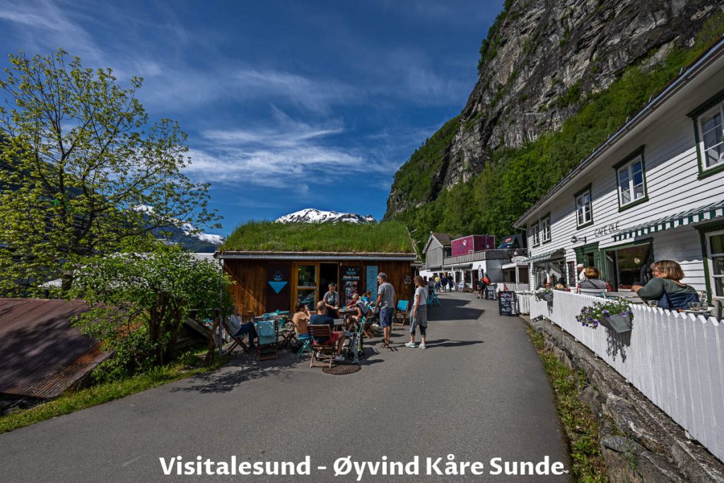 People walk at the Geiranger village promenade and sit in restaurants and cafes.