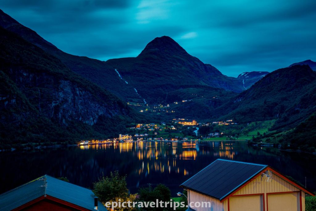 Night photo of Geiranger village, fjord, and mountains in the background.