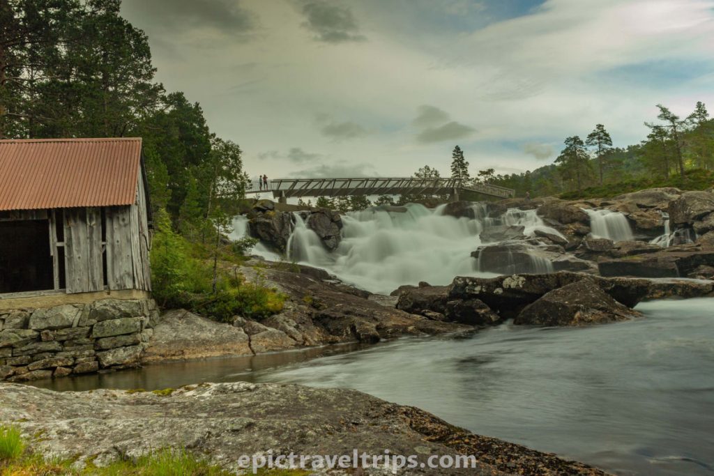 Likholefossen silky waterfall with a bridge and wooden house on the side in Norway.