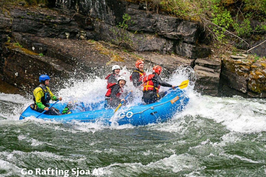 Sjoa river rafting with four persons paddling and one skipper at the back steering the raft while water splashing them in Norway.