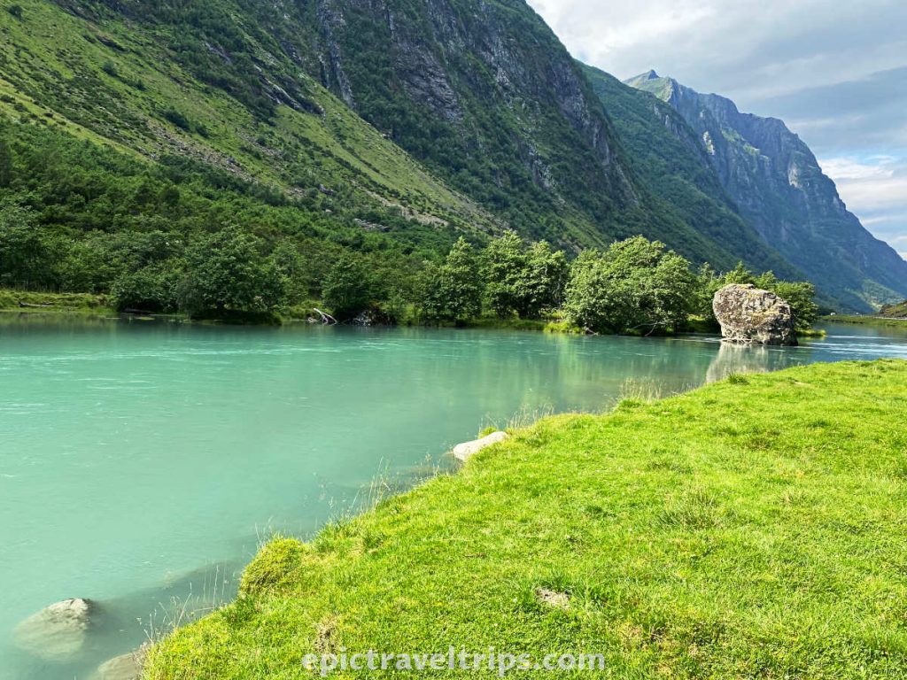 Stradalselva river with emerald green water and rock on the side, mountains at the back, and green grass in front, near Skei in Norway.