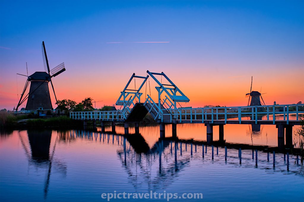 White lift bridge over the canal and Kinderdijk Windmills on the other side on sunset and blue hour photo in The Netherlands.