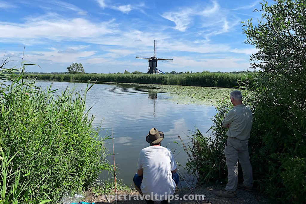 Fisherman on the canal and Museum Windmill Blokweer at Kinderdijkv in the background, The Netherlands.